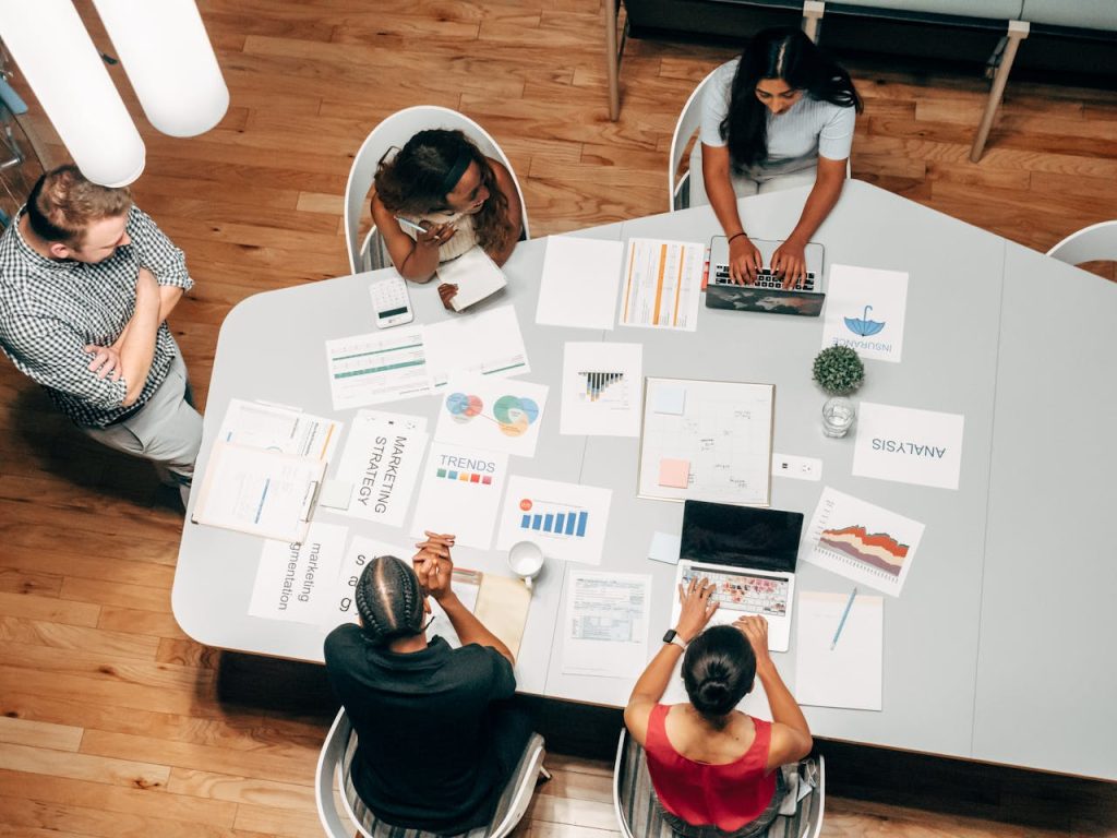 Diverse team collaborating around a table covered with marketing strategy documents, charts, and laptops in a modern office